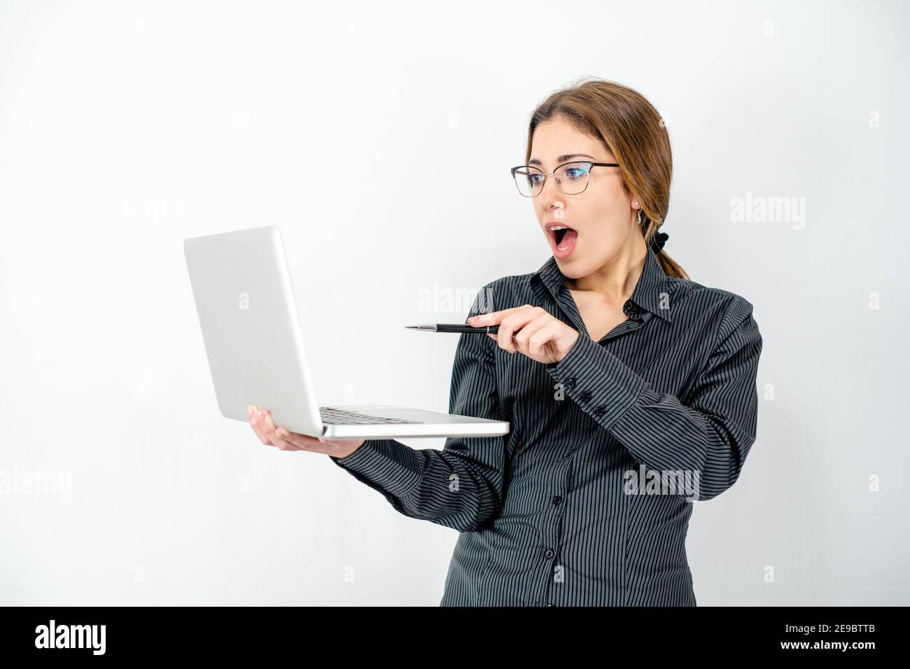 Überrascht isoliert schöne junge Frau posiert in Studie Schuss halten Laptop in der Hand zeigt mit Stift den Bildschirm tragen Büro Business Kleidung. Kau Stockfoto