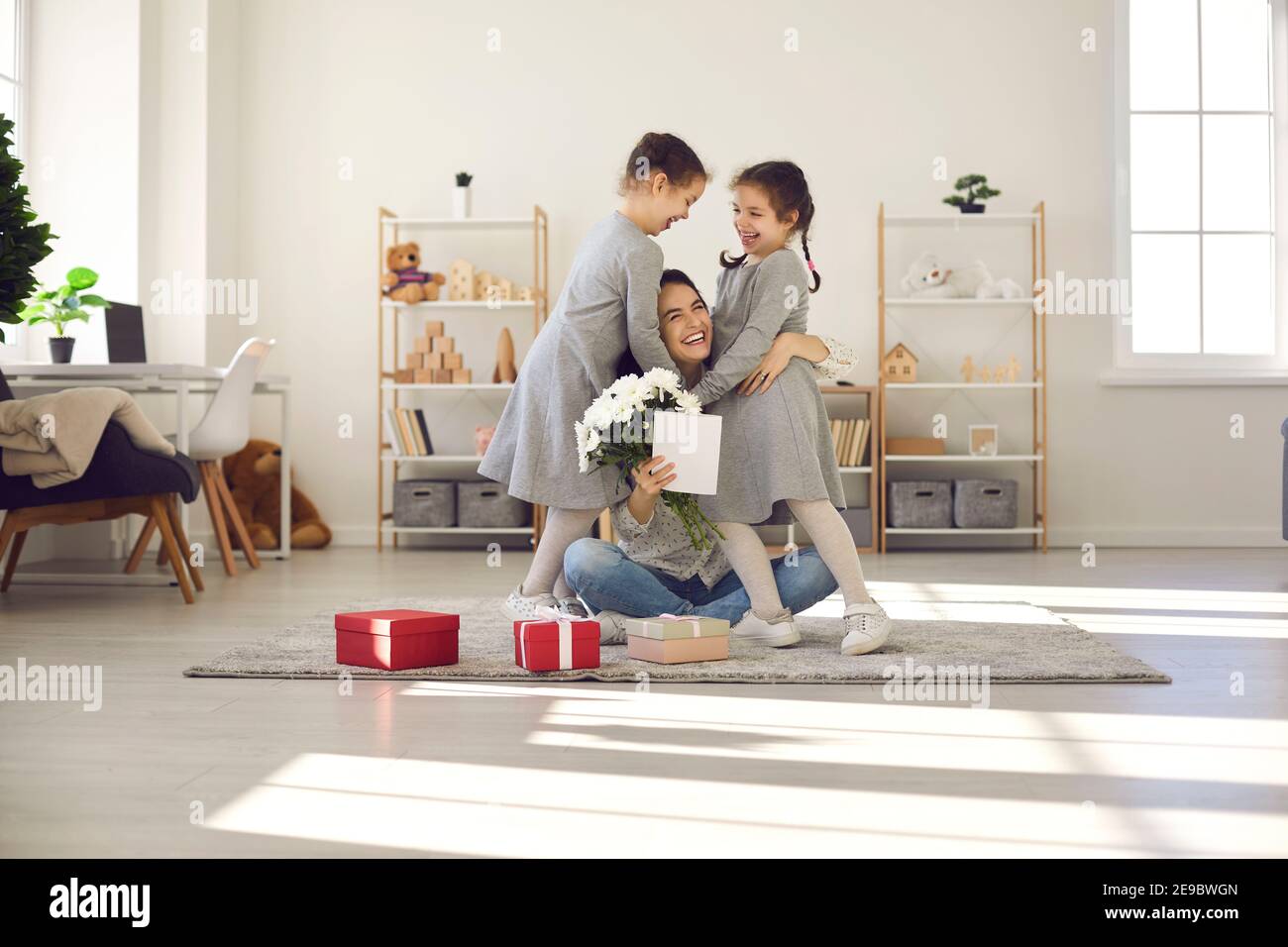 Glückliche Mutter umarmt ihre beiden Töchter zu Hause im Wohnzimmer, nachdem sie zum Muttertag gratuliert hat. Stockfoto