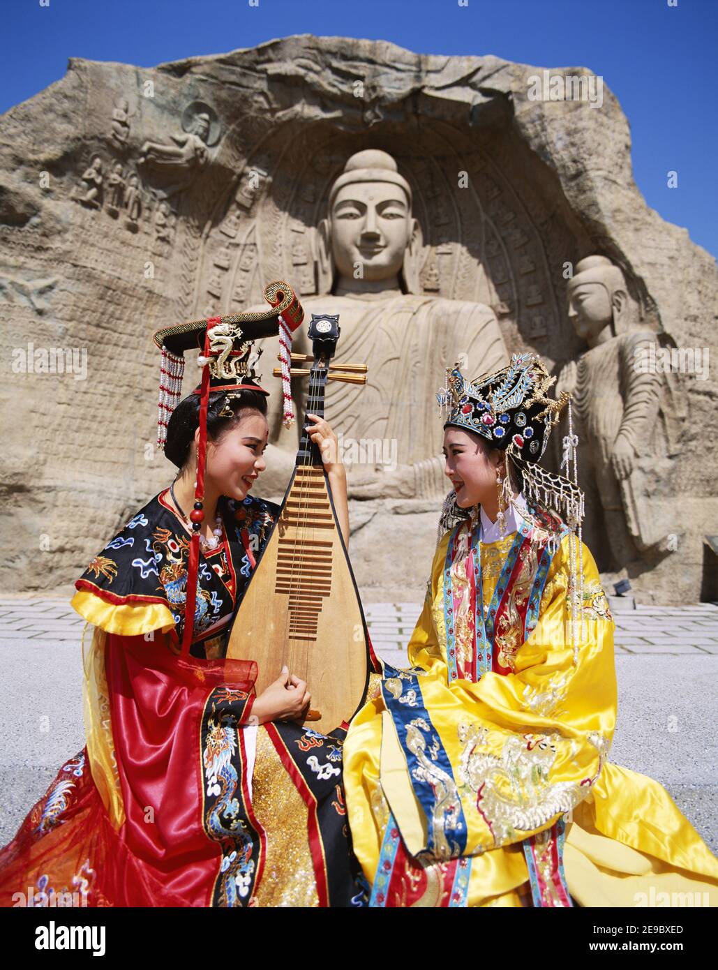 Asia China, Hong Kong, Mädchen in Tracht mit traditionellem Musikinstrument (dreisaitige Laute) und Buddha Statue im Hintergrund Stockfoto