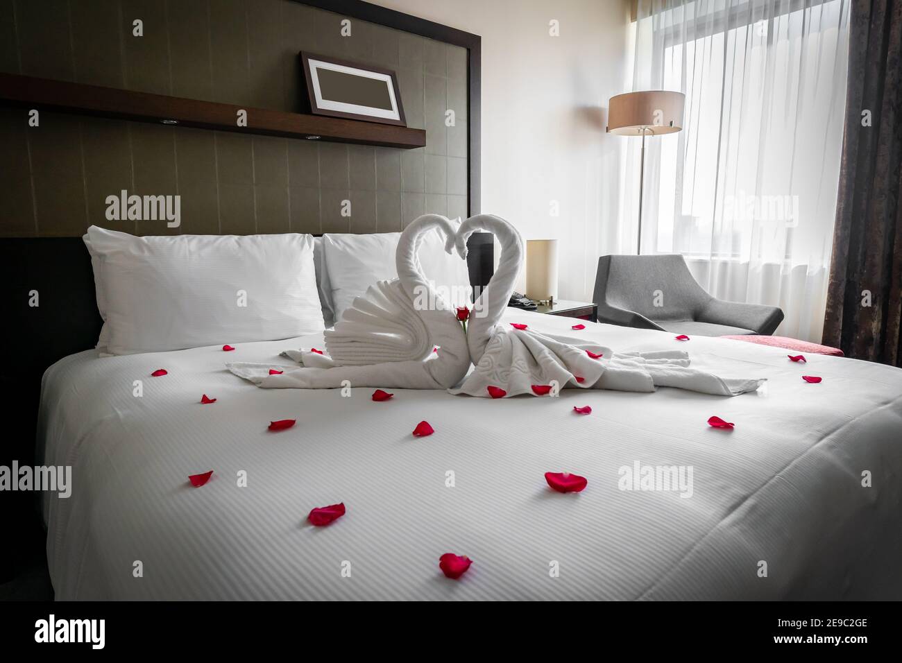 Romantisches, gemütliches Boutique-Hotel mit wunderschönen Schwanenhandtüchern Rote Rosenblätter auf dem Bett warten valentine Gäste auf Hochzeitstag für die Flitterwochen Stockfoto