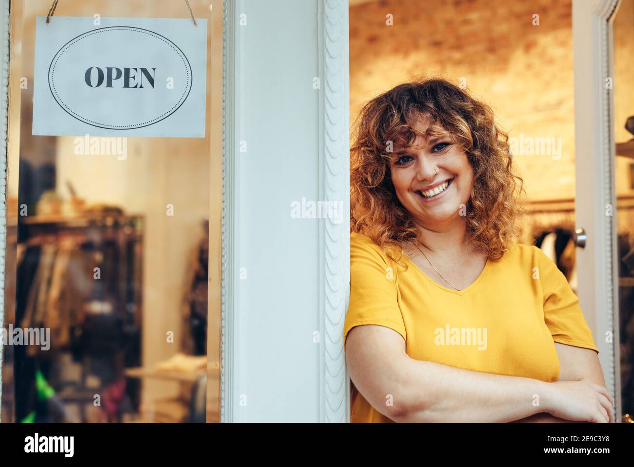 Porträt eines Bekleidungsladens Besitzer stehen an der Tür mit offenem Schild. Attraktive Bekleidungsgeschäft Besitzer steht in ihrem Shop Eingang. Stockfoto