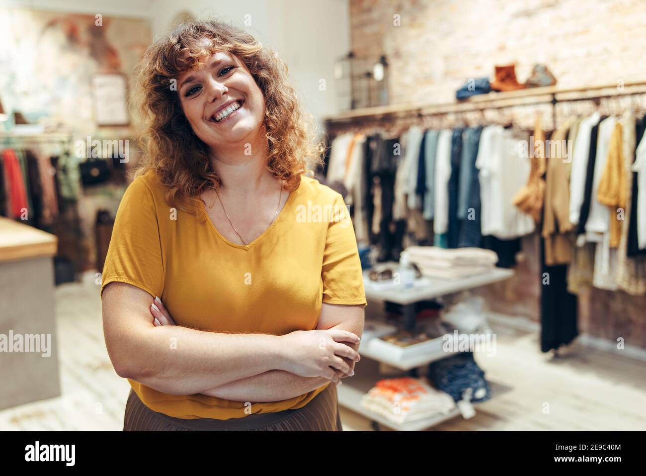 Portrait der attraktiven Kleidung Geschäft Besitzer stehend mit ihren Armen gekreuzt und lächelnd. Erfolgreicher Modehaus Besitzer. Stockfoto