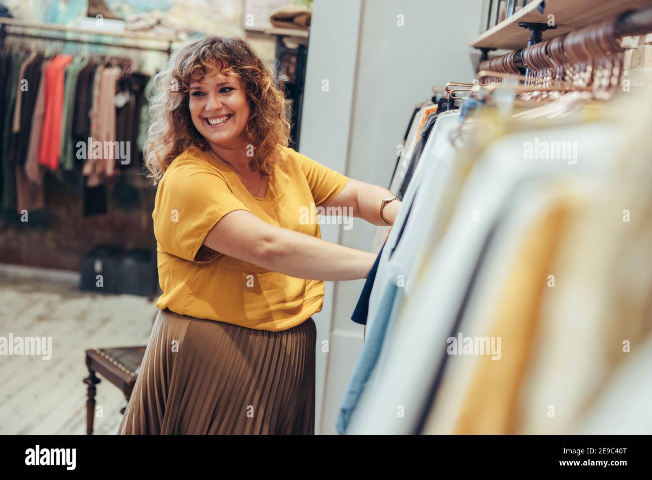Frau, die in einem Bekleidungsgeschäft arbeitet. Weibliche Besitzerin schaut weg und lächelt, während sie einem Kunden hilft, in einem Modeladen zu kaufen. Stockfoto