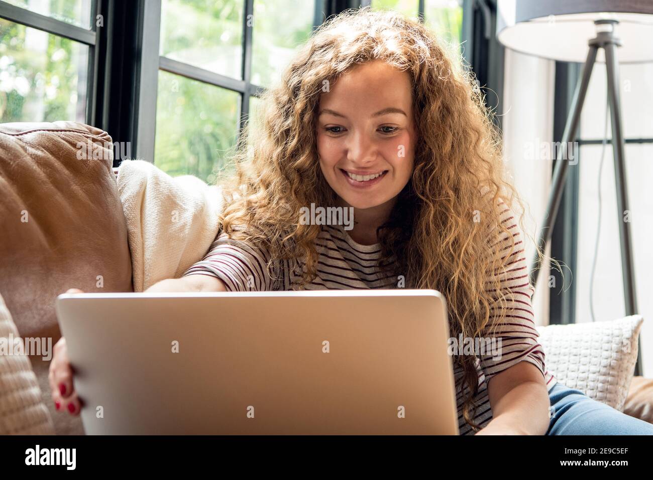 Ziemlich lächelnde kaukasische Frau macht Videoanruf mit Laptop-Computer Tagsüber auf der Couch im Wohnzimmer zu Hause Zeit Stockfoto