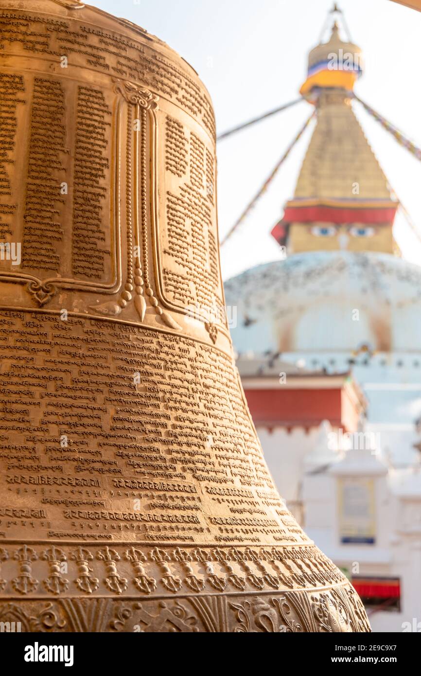 Kathmandu, Nepal - Januar 29 2021: Buddhistische Handschriften auf die goldene Glocke eingeschrieben mit Boudhanath Stupa im Hintergrund. Stockfoto