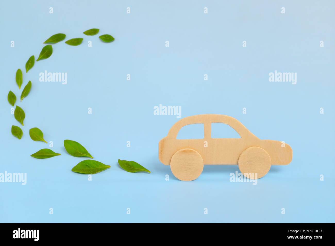 Holzauto Modell emittierende frische grüne Blätter auf blauem Hintergrund. Nachhaltige, saubere und grüne Energie sowie Biokraftstoff und Biodiesel für den Transport Stockfoto
