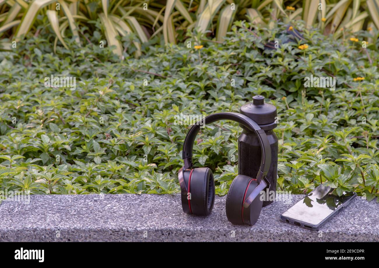Komposition von Smartphone und Kopfhörer zum Hören von Musik und Wasserflasche auf natürlichem grünem Hintergrund in der Ruhezeit platziert. Persönliche devi Stockfoto