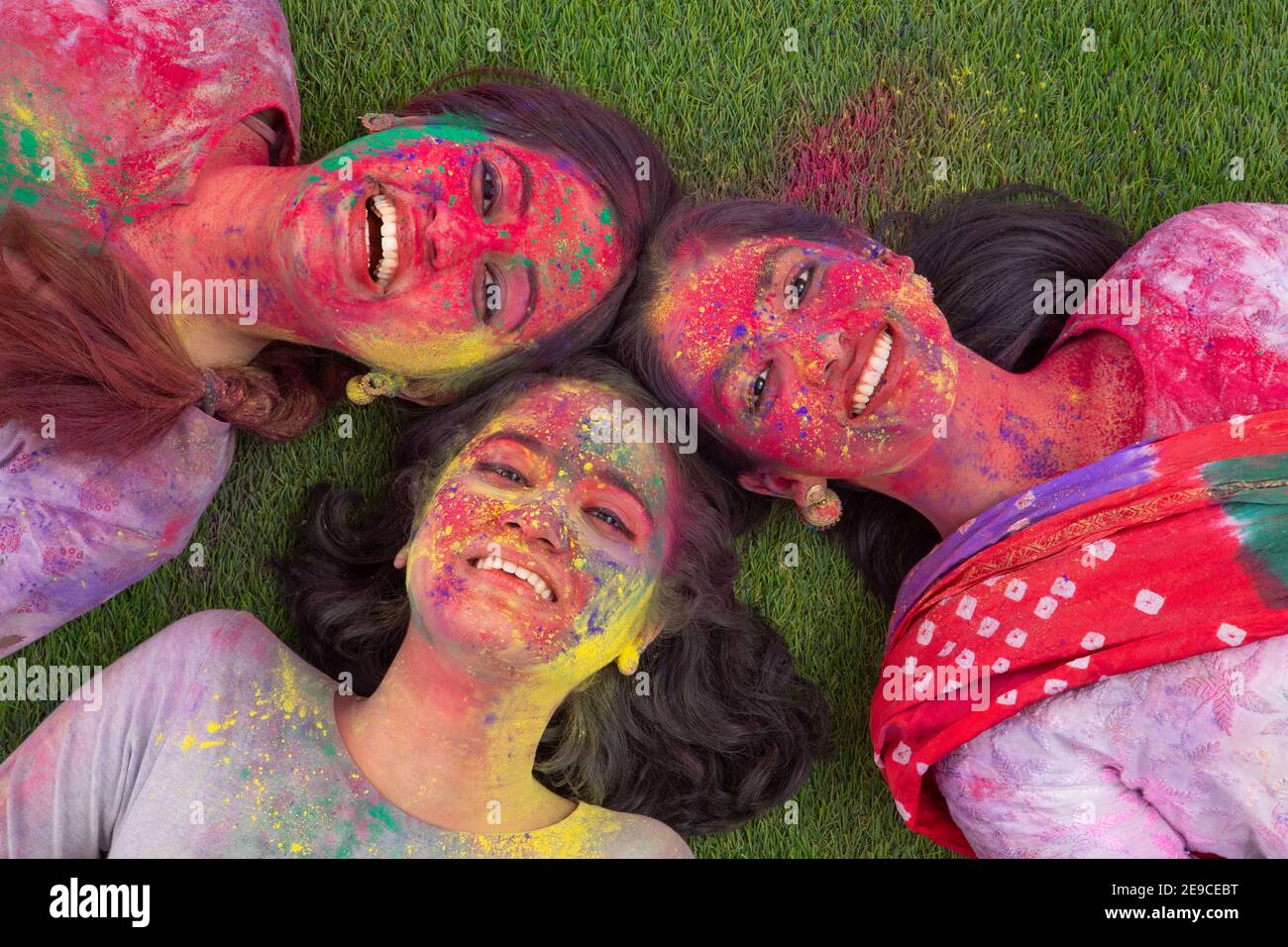 DREI JUNGE FRAUEN, DIE NACH DEM HOLI-SPIEL GLÜCKLICH AUF GRAS LIEGEN Stockfoto