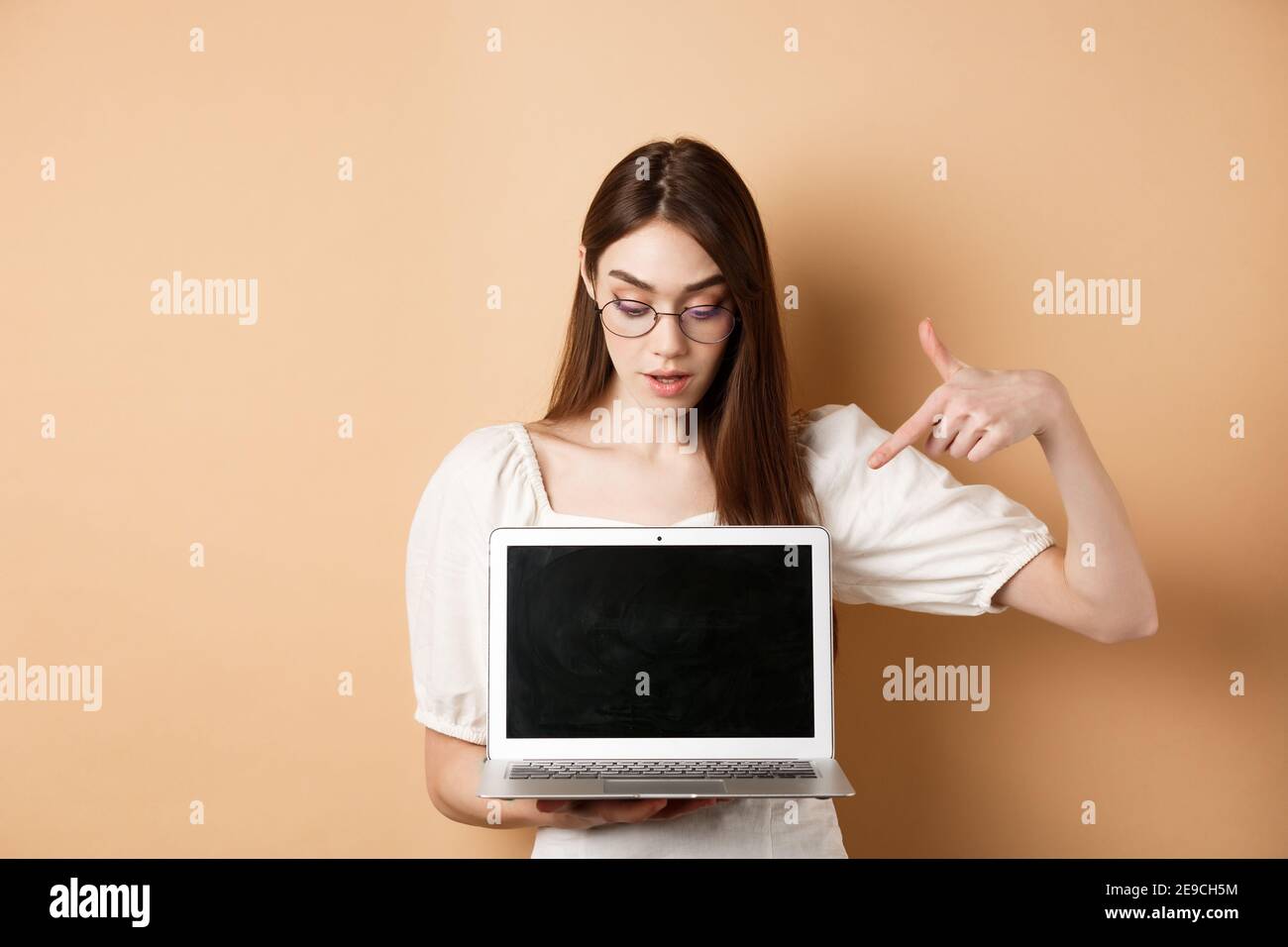 Neugieriges Mädchen in einer Brille zeigt auf Laptop-Bildschirm, überprüfen  Sie Online-Deal, zeigen Projekt auf Computer, auf beigem Hintergrund stehen  Stockfotografie - Alamy