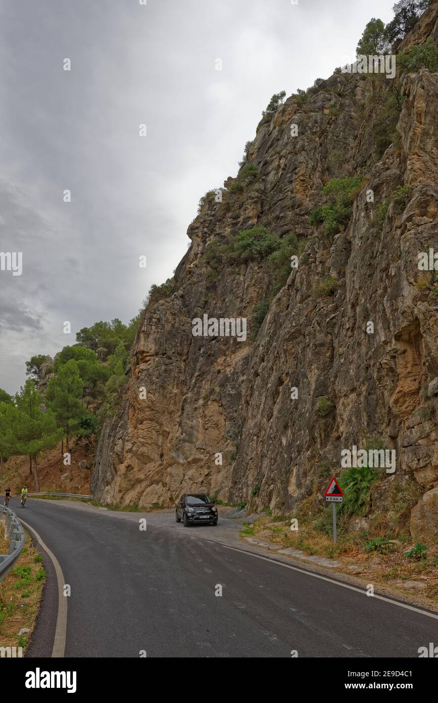 Ein schwarzes Fiat-Auto parkte in der Anhöhe einer kleinen spanischen Bergstraße, wobei zwei Radfahrer den sanften Hügel zwischen den Felswänden hinauffahren. Stockfoto