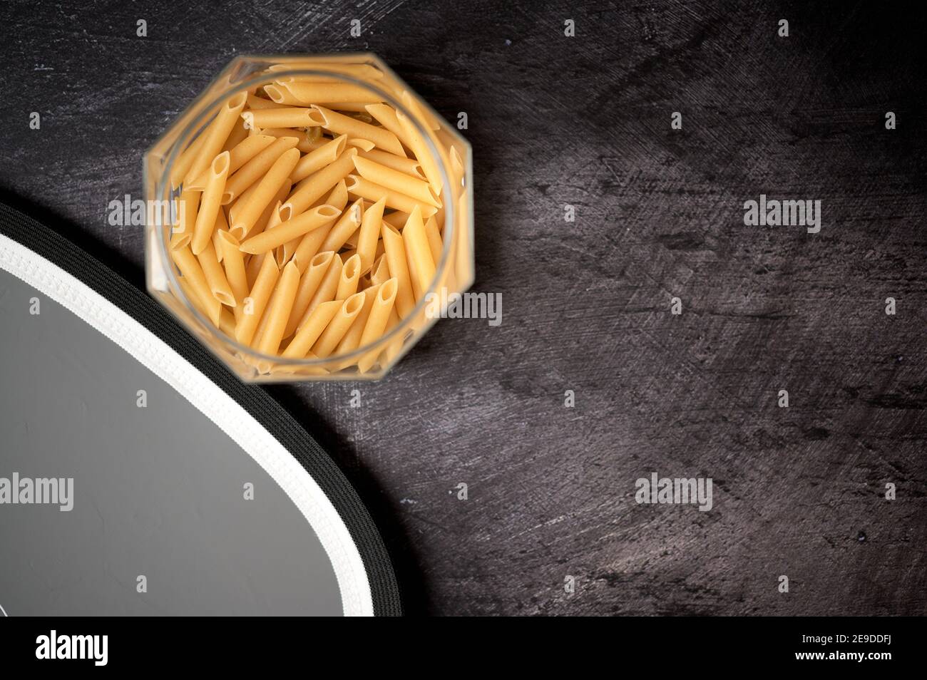 Detail eines Glas mit Macaroni Pasta offen auf Ein dunkler Hintergrund und eine graue Karte Stockfoto