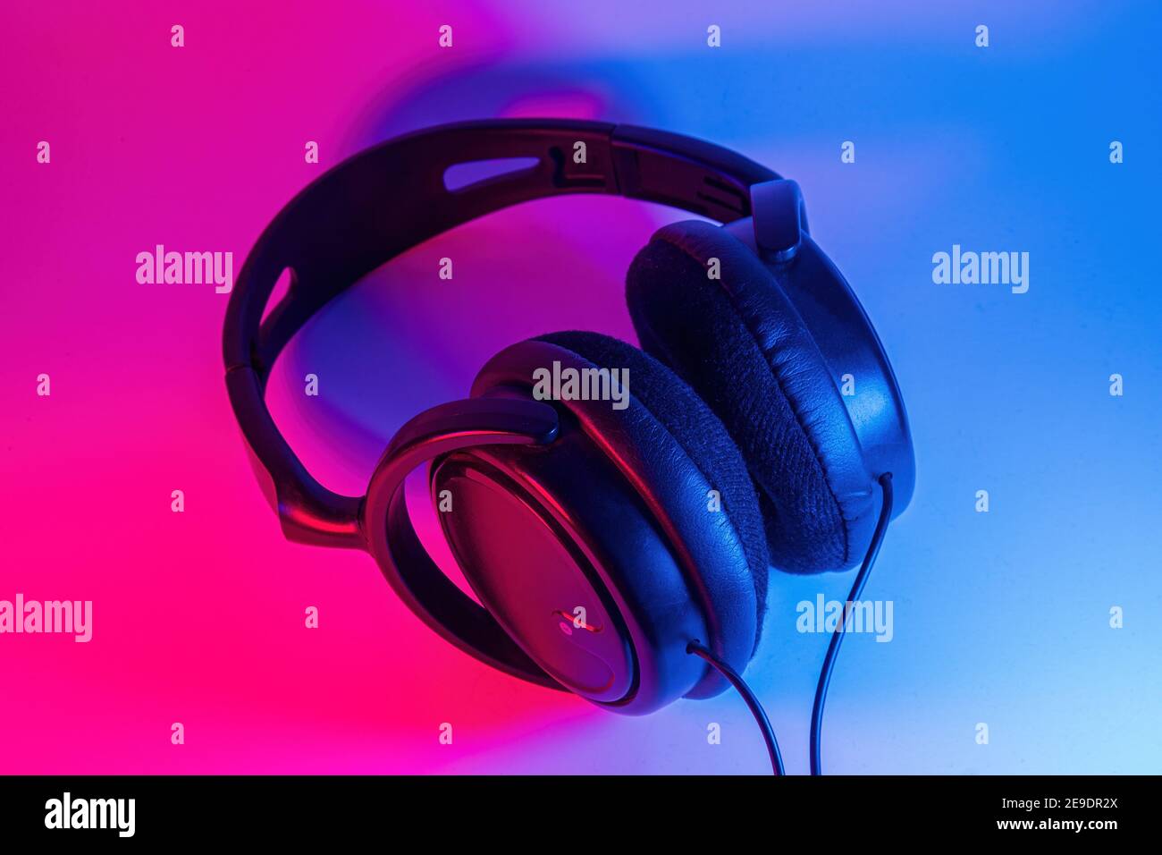 Elegante schwarze kabellose Kopfhörer mit farbenfrohem Neonlicht auf abstraktem Hintergrund isoliert. Modernes Technologiekonzept mit Kopierraum Stockfoto