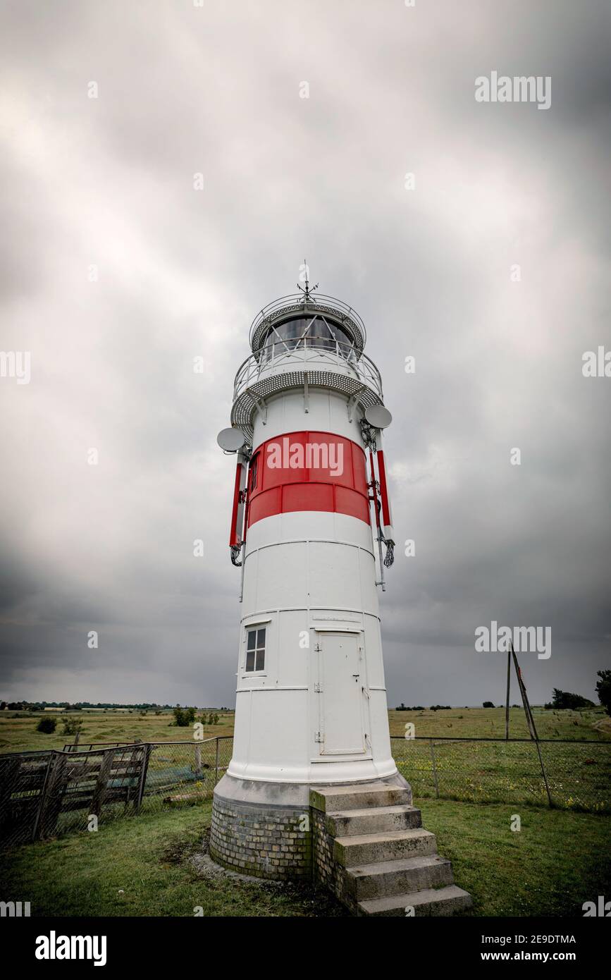 Kleiner Leuchtturm auf einem grünen Feld bei bewölktem Wetter mit Treppenstufen bis zu einer Tür Stockfoto