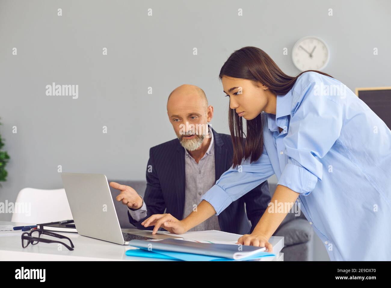 Junge Büroangestellte, die dem älteren männlichen Kollegen hilft, das Problem auf dem Laptop zu lösen. Stockfoto