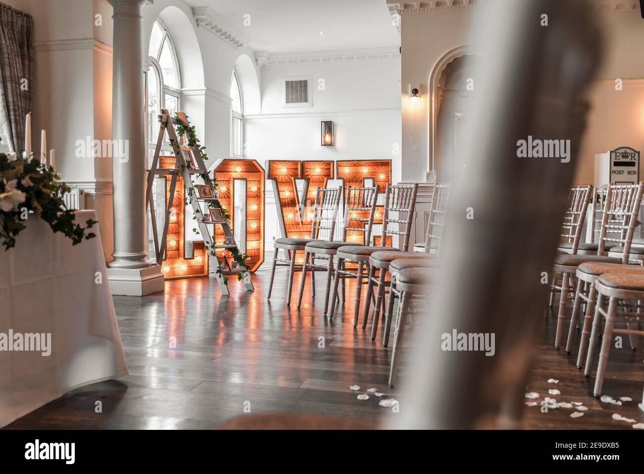 Hochzeit groß groß Liebe Großbuchstaben Holz rustikal beleuchtet auf Tanzfläche des wunderschönen Zeremonienraumes leuchtet orange Stockfoto