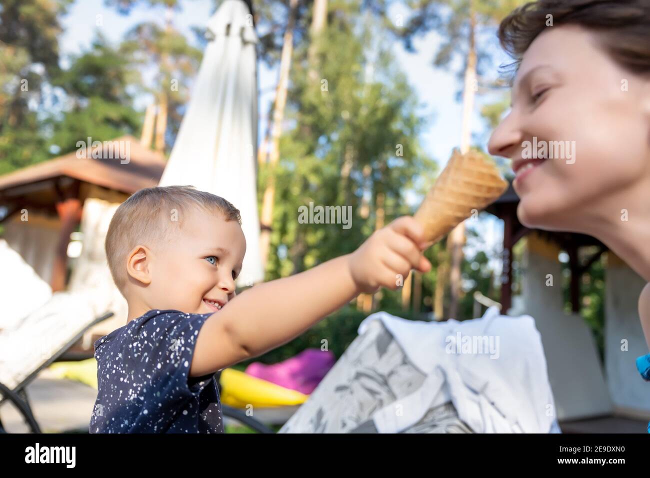 Kleine niedliche liebenswert verspielt kaukasischen blonde Kleinkind Junge Kind teilen süß lecker Eis mit Mama an heißen Sommertag im Freien. Zwei glückliche Menschen genießen Stockfoto