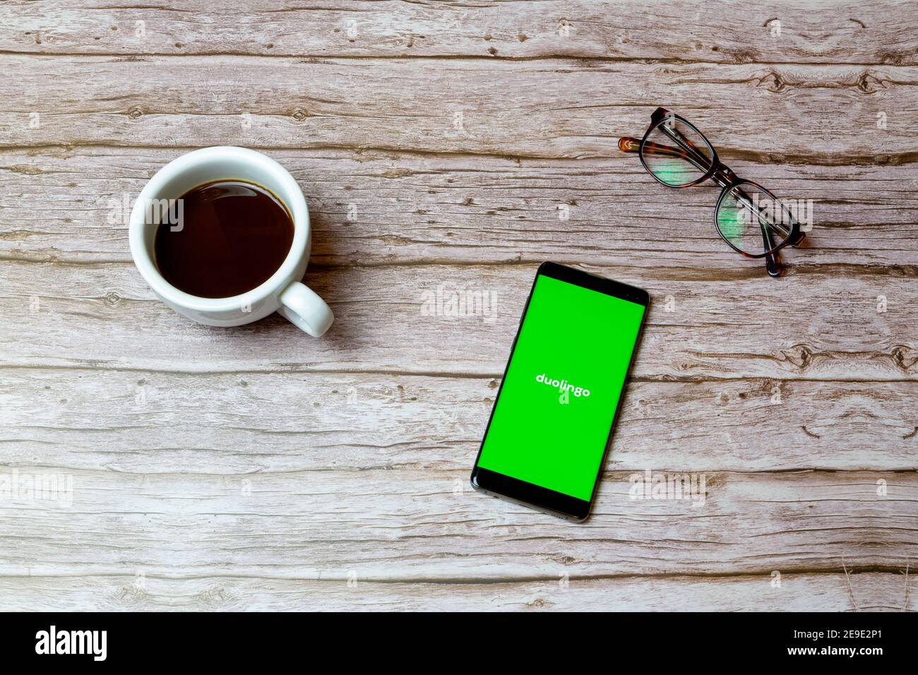 Ein Mobiltelefon oder Mobiltelefon auf einem Tisch Oder Schreibtisch mit der App Duolingo offen und einen Kaffee Daneben Stockfoto