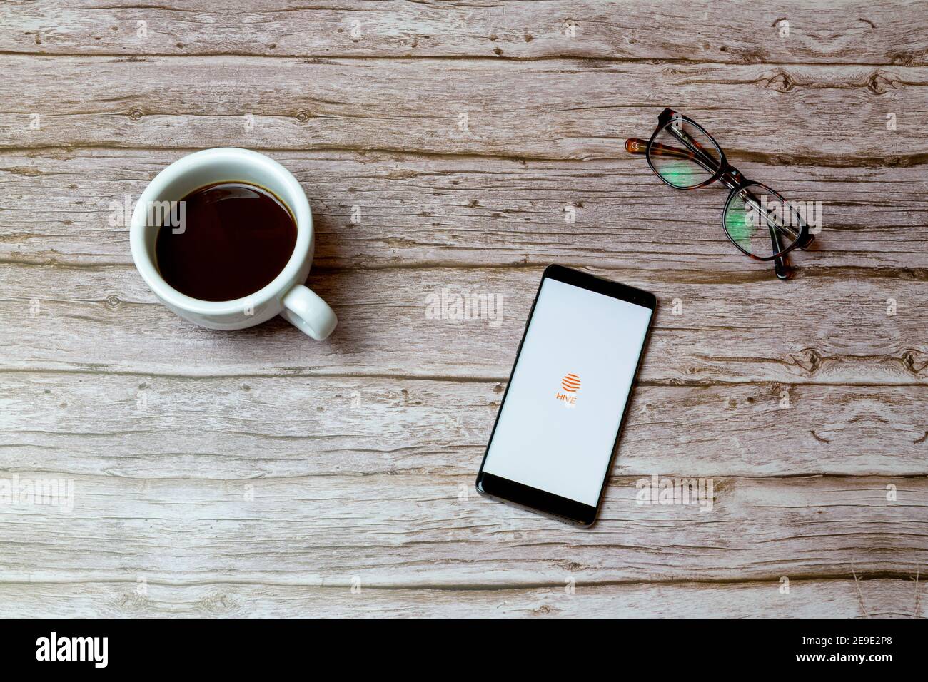 Ein Mobiltelefon oder Mobiltelefon auf einem Tisch Oder Schreibtisch mit der Hive Energy App geöffnet und ein Kaffee daneben Stockfoto