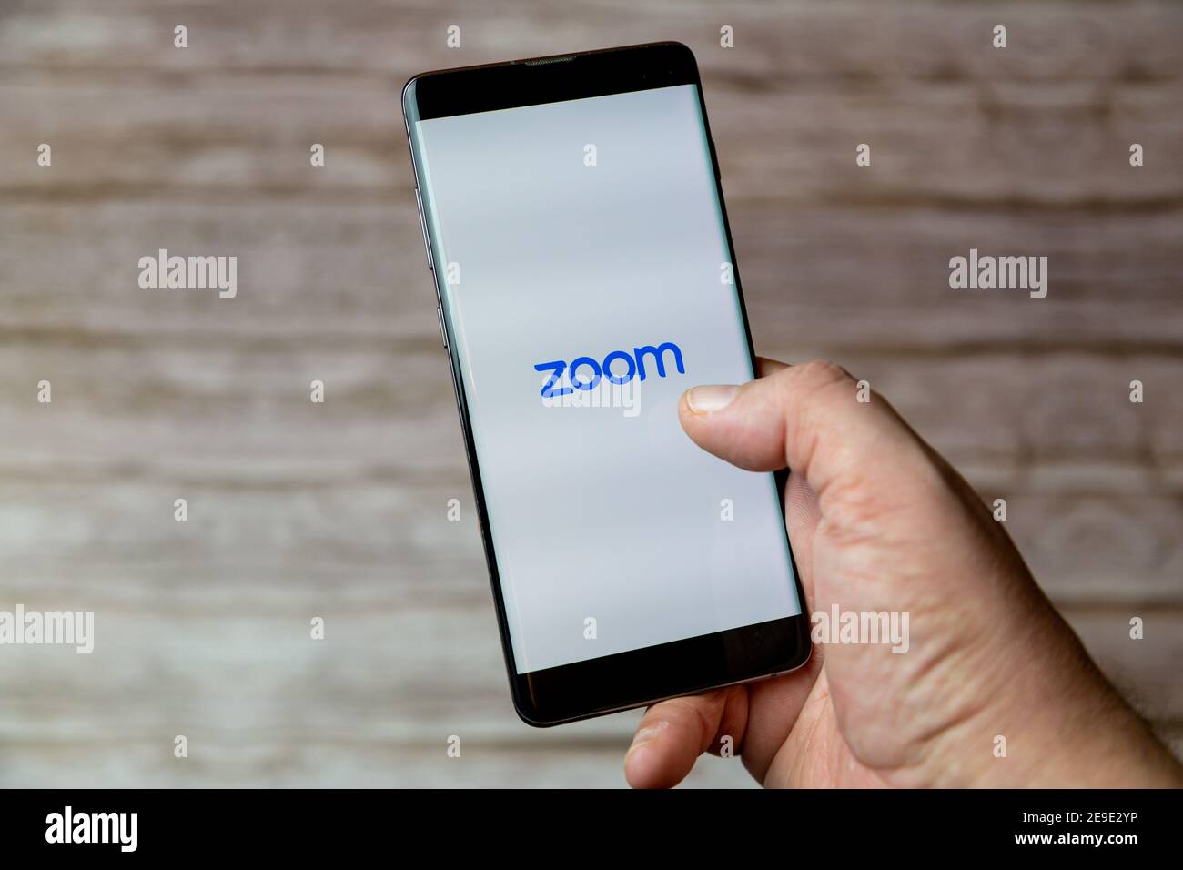 Eine Hand, die ein Mobiltelefon oder Mobiltelefon mit hält Die Zoom Calling App auf dem Bildschirm Stockfoto