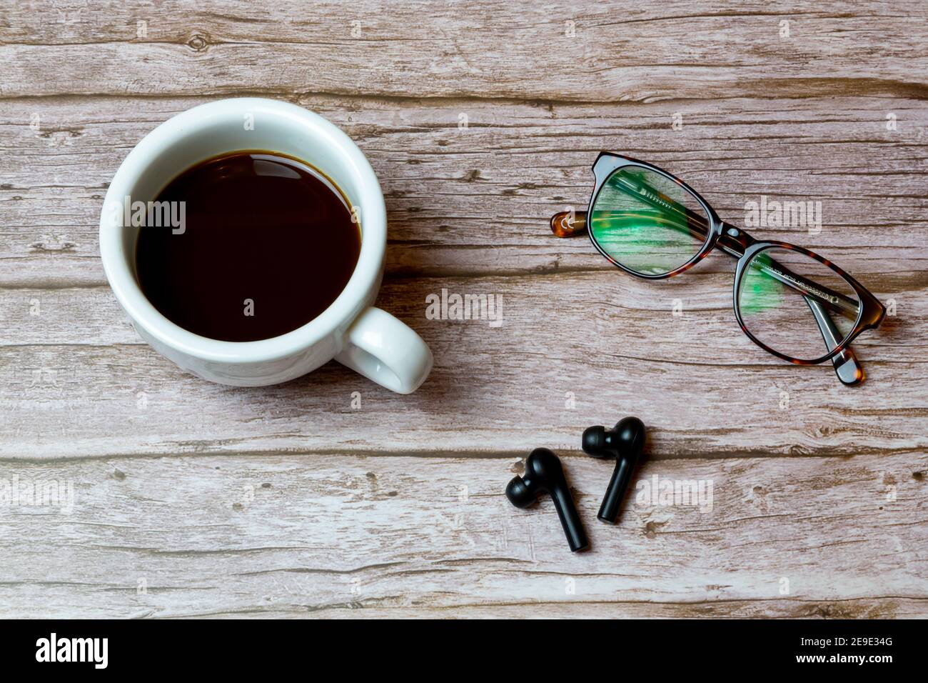 Schnurlose Ohrhörer auf einem Holztisch Oder Schreibtisch neben einem Kaffee und ein paar Gläser Stockfoto