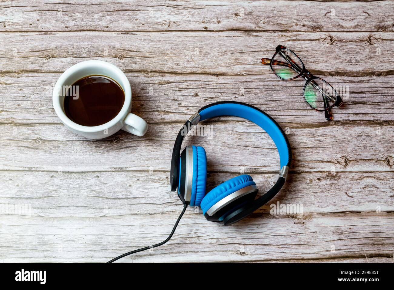 Ein Paar über Ohr kabelgebundene Kopfhörer auf einem gelegt Holztisch oder Schreibtisch neben einem Kaffee und einem Brille Stockfoto