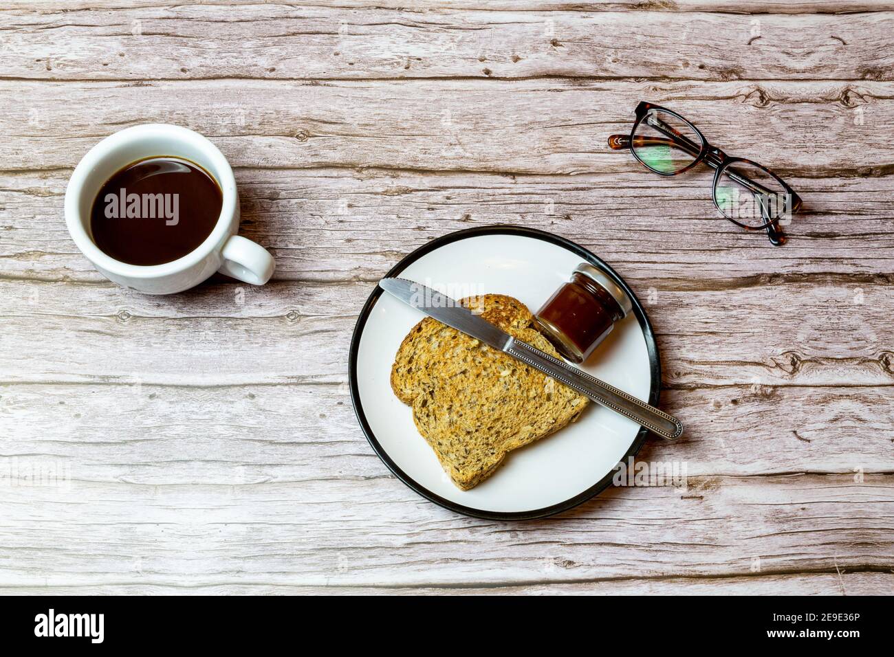 Toast und Marmelade auf einem Teller neben einem Kaffee Auf einem Holztisch, um die Frühstückszeit darzustellen Stockfoto