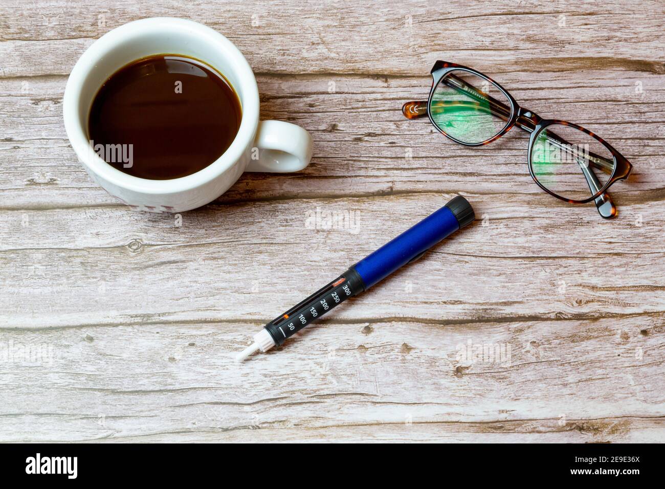 Ein Insulin-Stift für Diabetiker auf einem Holztisch oder Schreibtisch Neben einer Tasse Kaffee, um den Morgen darzustellen Injektion von Insulin Stockfoto