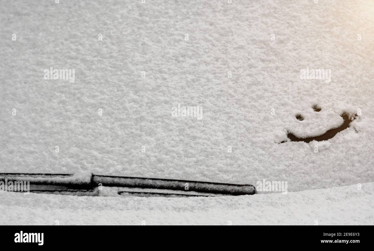 Schneehintergrund. Textur von nassem Schnee mit einem fröhlichen Smiley-Symbolmuster im Winterfenster des Autos im Nahbereich. Lächeln Sie im Schnee, glücklich Stockfoto