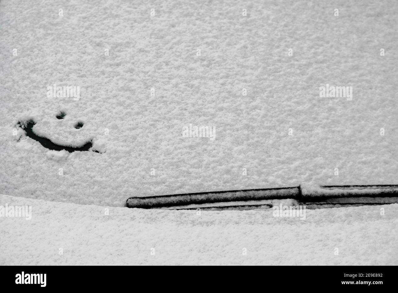 Schneehintergrund. Textur von nassem Schnee mit einem fröhlichen Smiley-Symbolmuster im Winterfenster des Autos im Nahbereich. Lächeln Sie im Schnee, glücklich Stockfoto