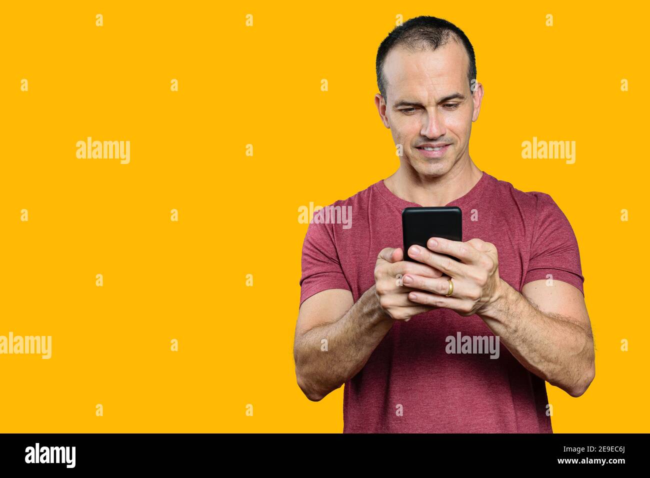 Reifer brasilianischer Mann hält sein Smartphone und lächelt. Orangefarbener Hintergrund. Stockfoto