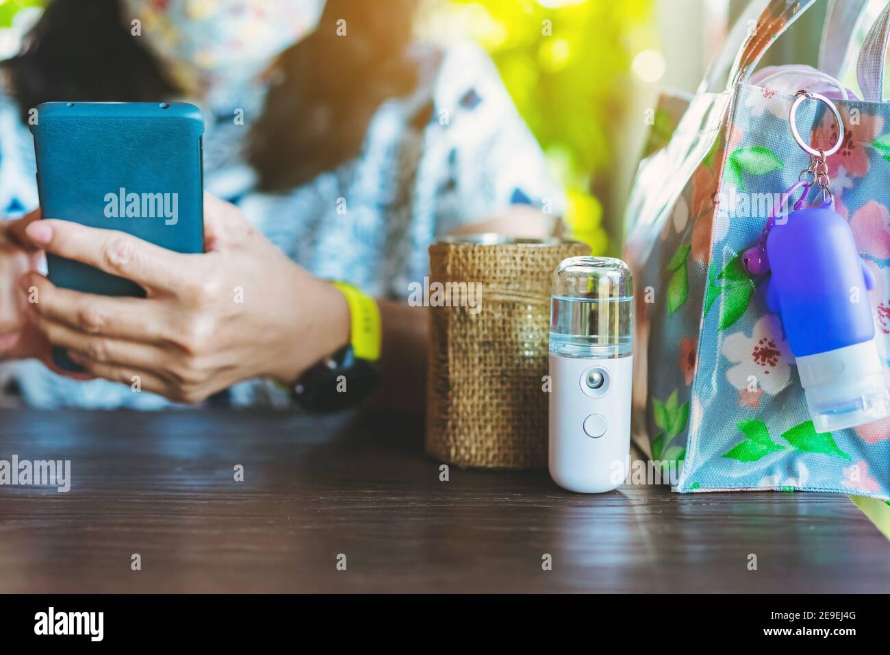 Alkohol-Nano-Sprüher für die Handreinigung, um die zu verhindern Ausbreitung des Corona-Virus (Covid-19) auf den Tisch gelegt mit Verschwommenes Bild der Frau verwenden mobil Stockfoto