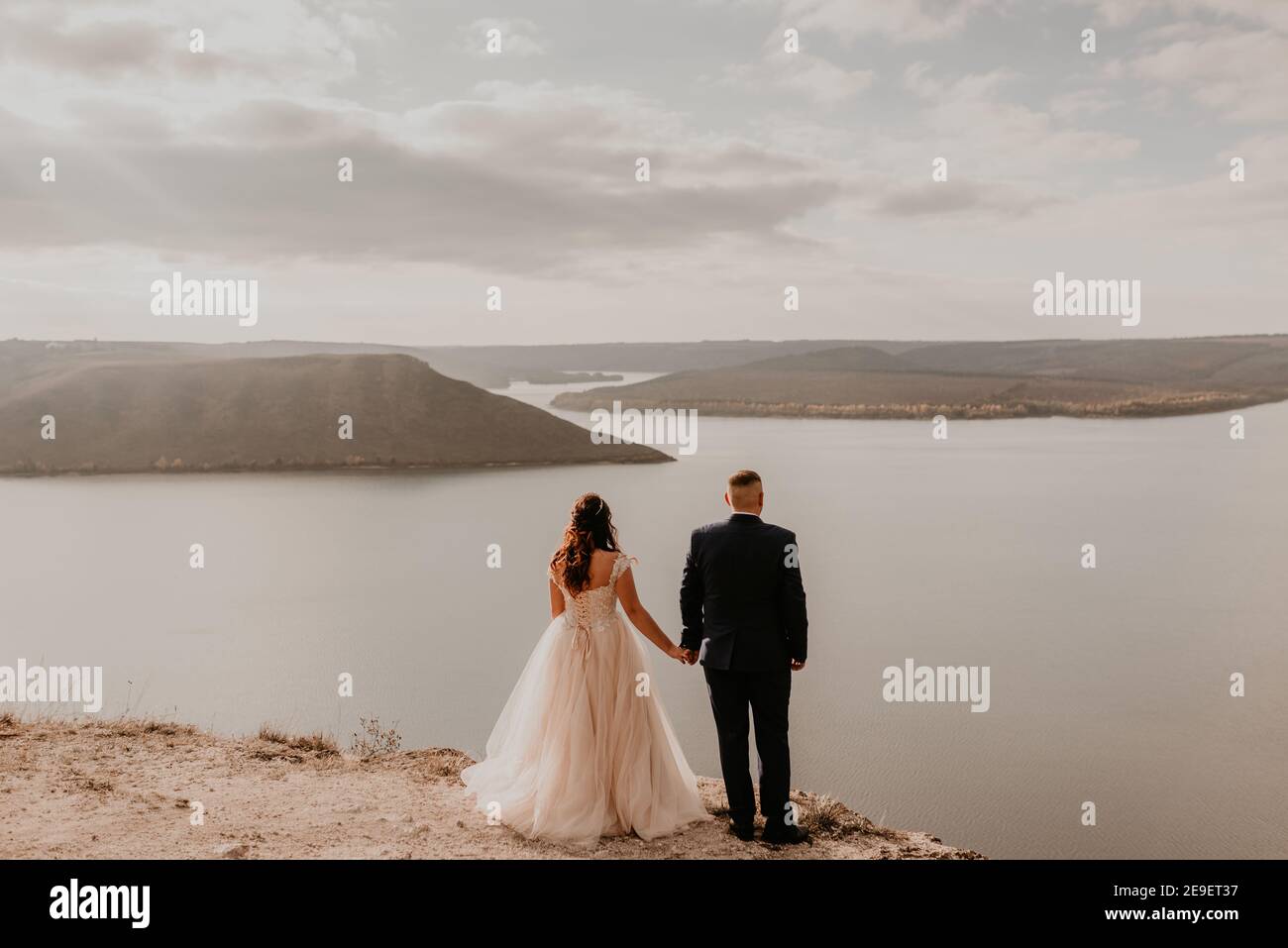 Liebevolles Paar Hochzeit Brautpaar in weißem Kleid und Anzug Spaziergang im Sommer auf dem Berg über dem Fluss. Sonnenuntergang und Sonnenaufgang. Mann und Frau auf Felsen über der Klippe Stockfoto