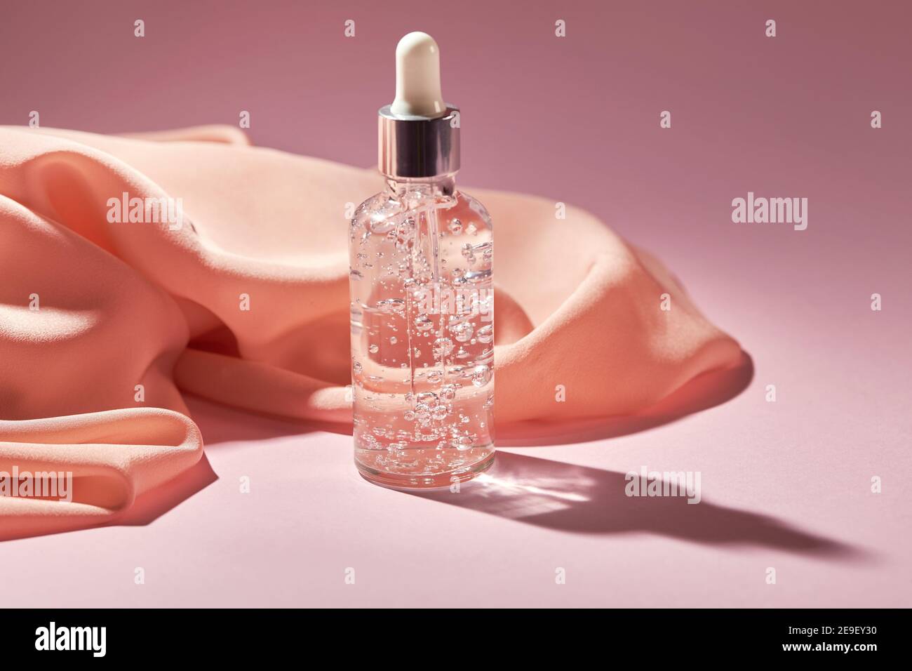 Anti-Aging-Serum in einer Glasflasche auf einem rosa Hintergrund mit Seidenschal. Flüssiges Gesichtsserum mit Kollagen und Peptiden. Frühlingspflege für Haut Konzept Stockfoto