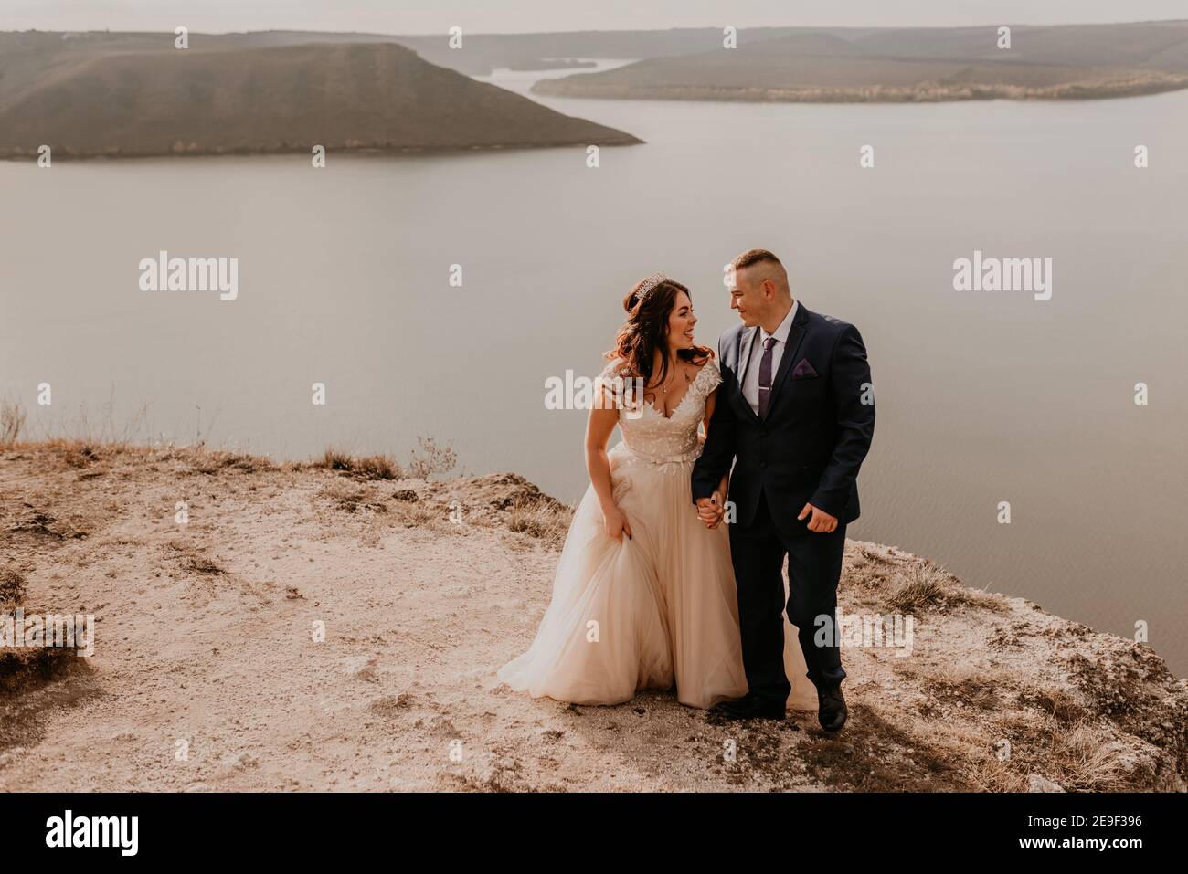 Liebevolles Paar Hochzeit Brautpaar in weißem Kleid und Anzug Spaziergang im Sommer auf dem Berg über dem Fluss. Sonnenuntergang und Sonnenaufgang. Mann und Frau auf Felsen über der Klippe Stockfoto