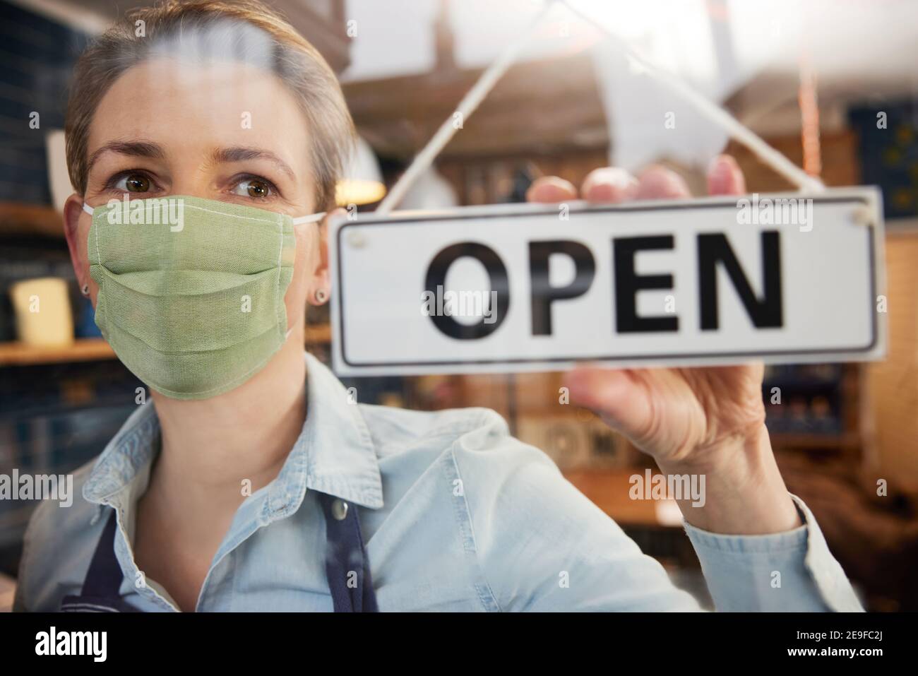 Weibliche Besitzerin Von Kleinunternehmen Trägt Gesichtsmaske Drehen Runde Open Sign Während Der Gesundheitsinpandemie Stockfoto