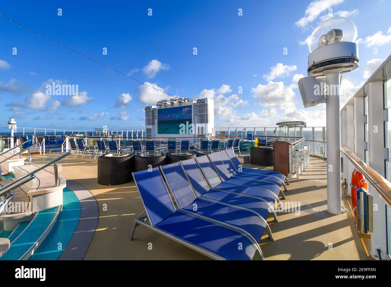 Ein leeres Kreuzfahrtschiff-Oberdeck mit Medienbildschirm und Liegestühlen am Meer an einem sonnigen Tag. Stockfoto