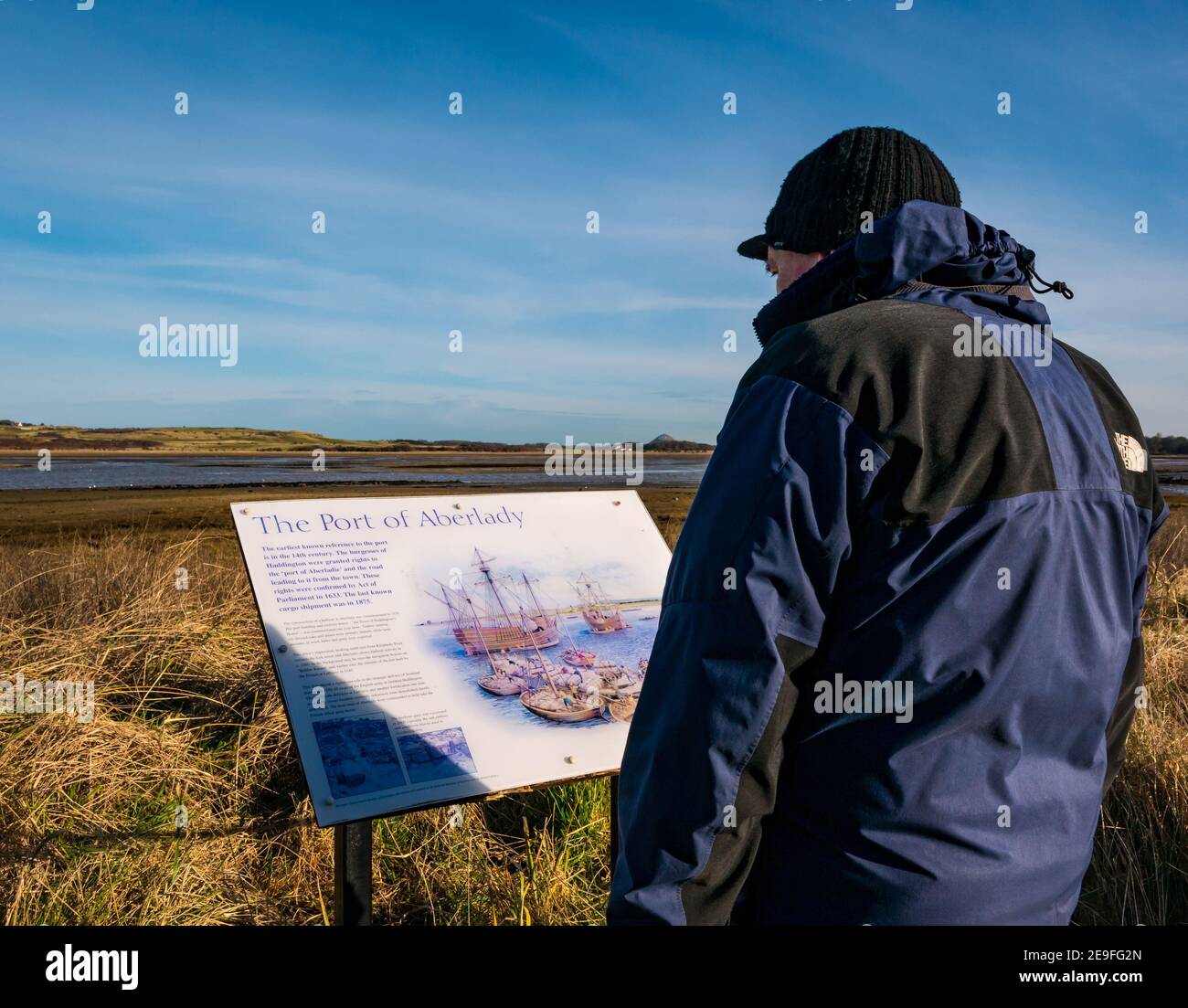 Mann, der an einem kalten, sonnigen Tag die lokalen Informationen über die Geschichte anschaut, Aberlady Bay Nature Reserve, East Lothian, Schottland, Großbritannien Stockfoto