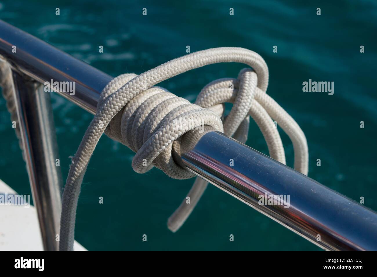 Detail des weißen Seiles, das in einem marinen Knoten auf gespannt ist Bootsgeländer aus Edelstahl Stockfoto