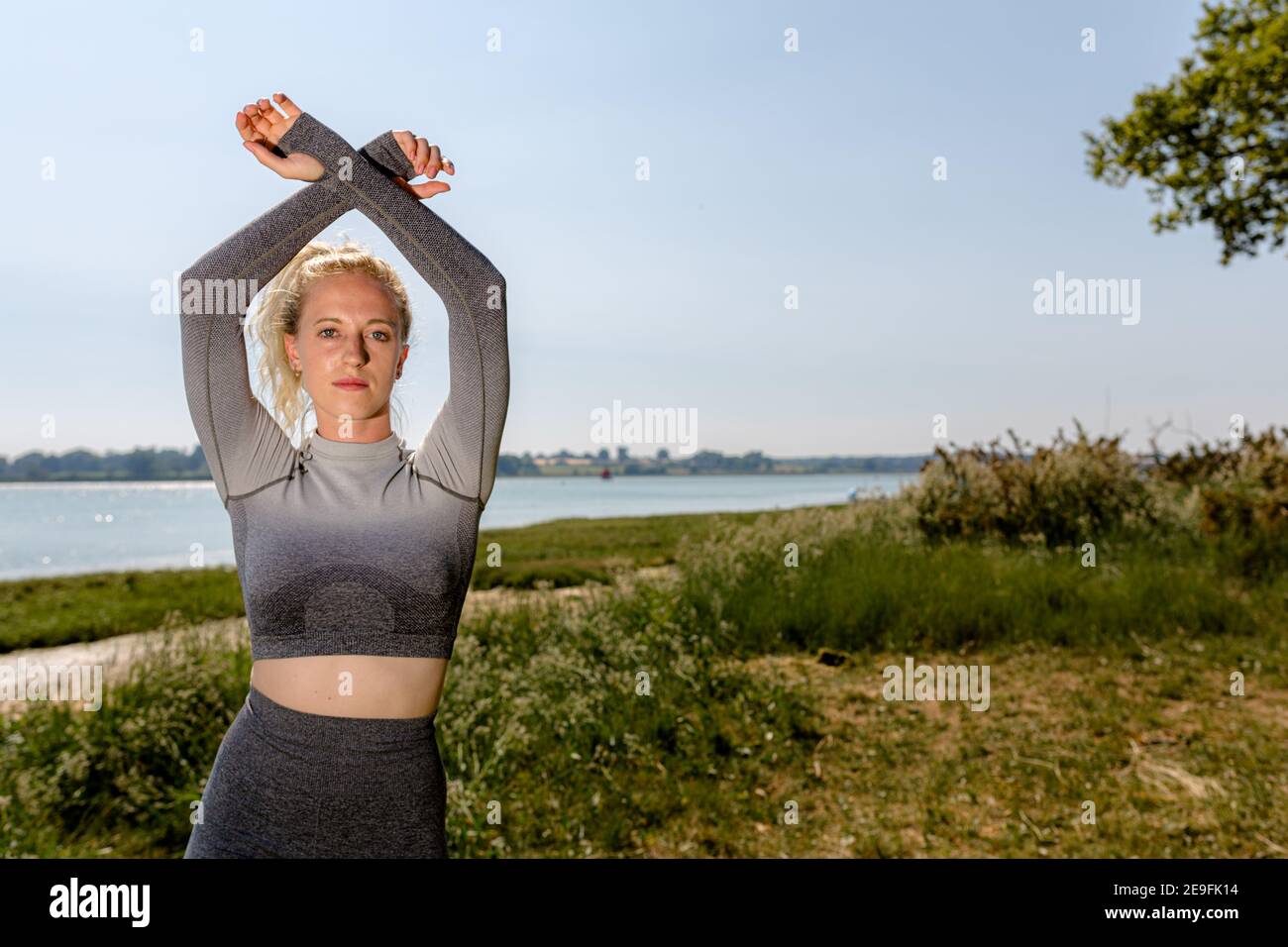 Attraktive Passform junge Frau in Sportkleidung bereit, in der Sonne am Flussufer zu trainieren. Gesundes Lifestyle-Konzept Stockfoto