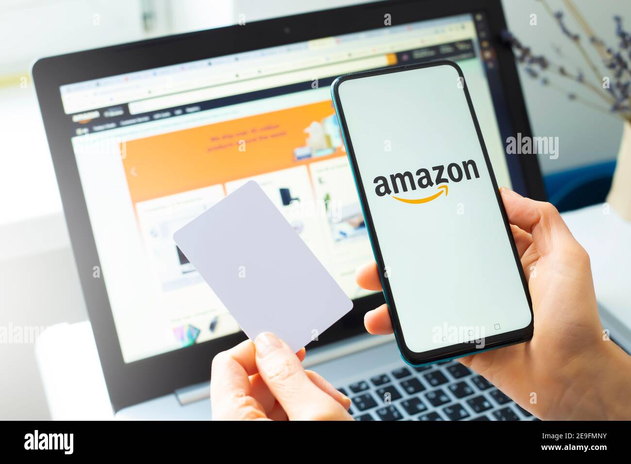Kiew, Ukraine - 02. Februar 2021: Kauf von Waren im Amazon Online-Shop mit einem Smartphone und Laptop und einer Kreditkarte. Stockfoto