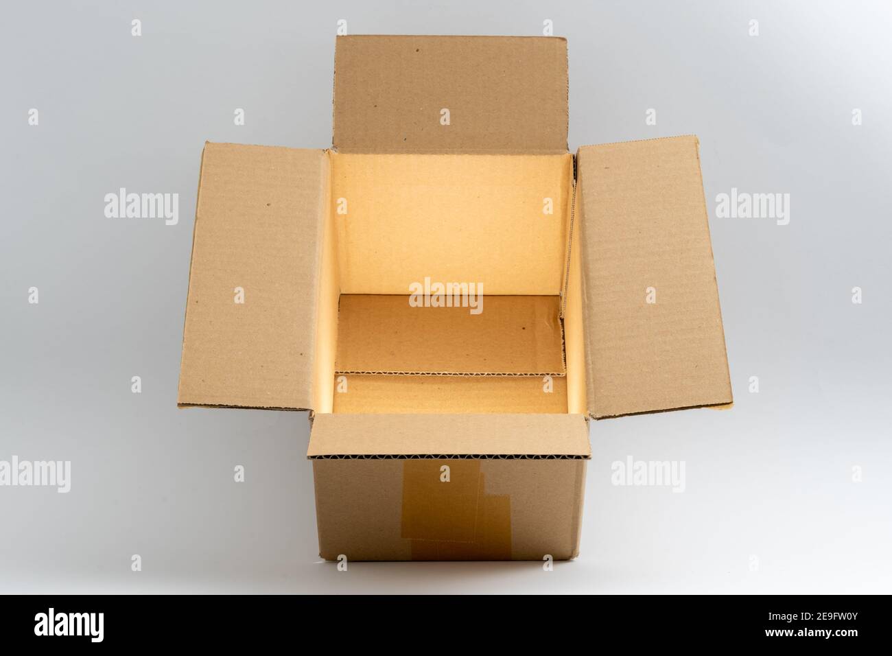 Geöffnete Kartonverpackung mit mystisch glänzendem goldenem Licht vor einem sauberen weißen Hintergrund. Ein brauner Karton, der für den Versand und Delive verwendet wird Stockfoto