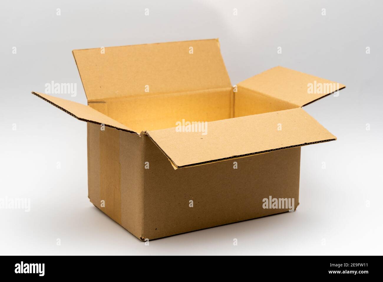 Geöffnete Kartonverpackung mit mystisch glänzendem goldenem Licht vor einem sauberen weißen Hintergrund. Ein brauner Karton, der für den Versand und Delive verwendet wird Stockfoto