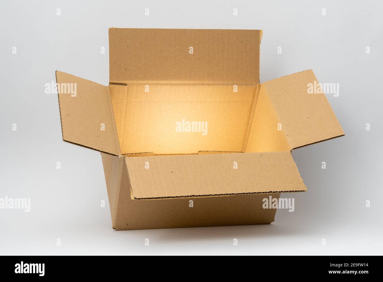 Geöffnete Kartonverpackung mit mystisch glänzendem goldenem Licht vor einem sauberen weißen Hintergrund. Ein brauner Karton, der für den Versand und Delive verwendet wird Stockfoto
