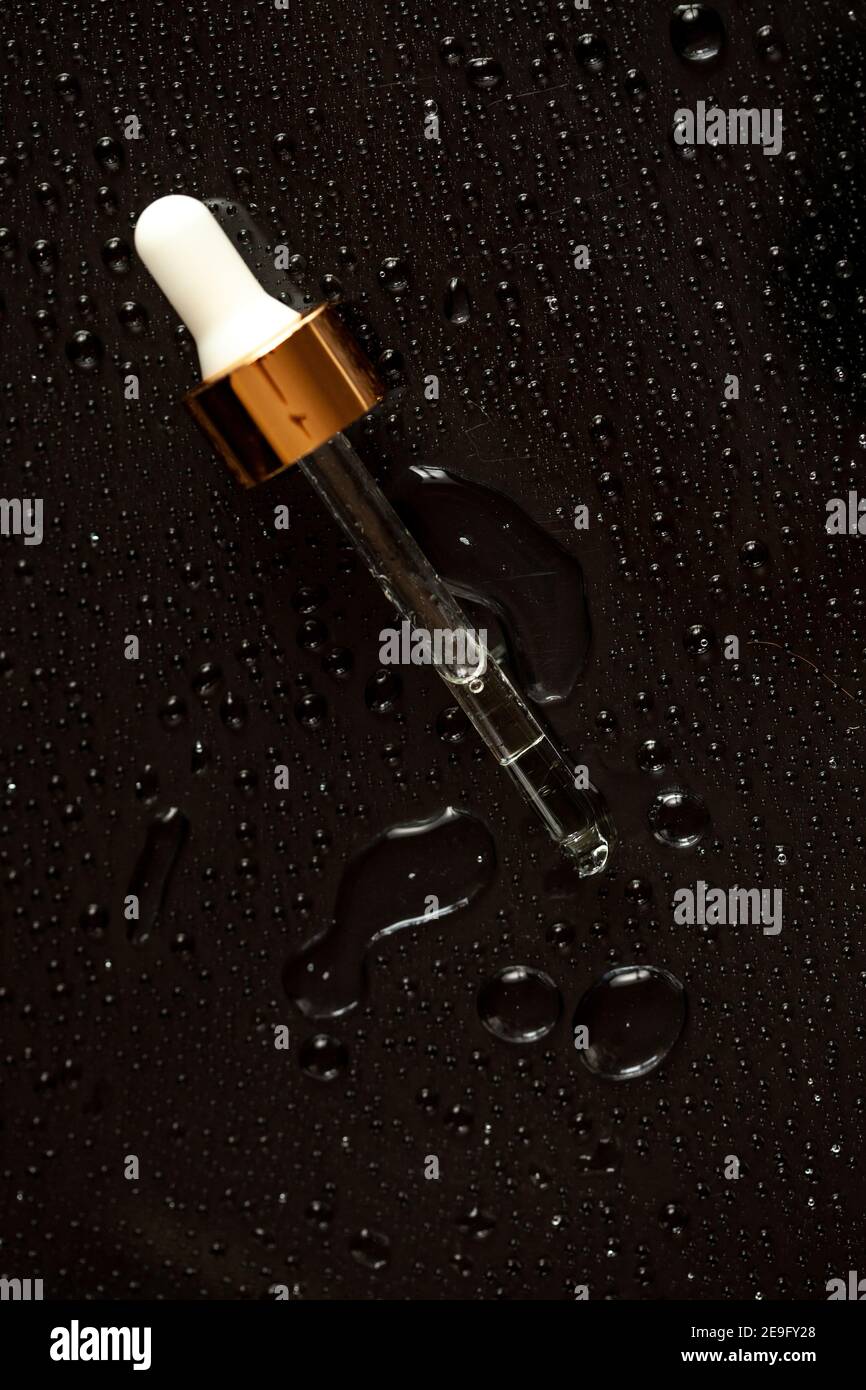 Glasflasche mit Medikamententropfer auf schwarzem und blauem Hintergrund mit Tropfen Flüssigkeit und Spritzern auf reflektierende Oberfläche. Medizinische Labortests. ICH Stockfoto