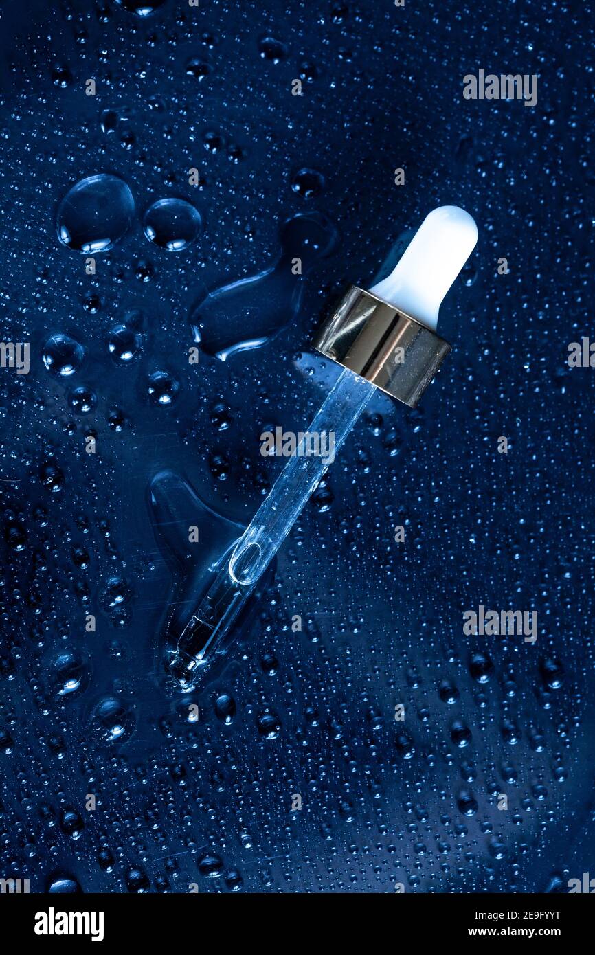Feuchtigkeitsspendende Beauty-Produkte Konzept - klassisch blauer Hintergrund mit Medizin Pipette und Wasser spritzt um ihn herum Stockfoto