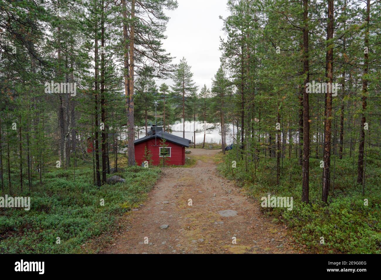 Weg zu einem schönen roten Holzhaus neben einem atemberaubenden See. Abgelegene einsame Hütte in Inari, Lappland, Finnland im grünen Kiefernwald. Autark Stockfoto
