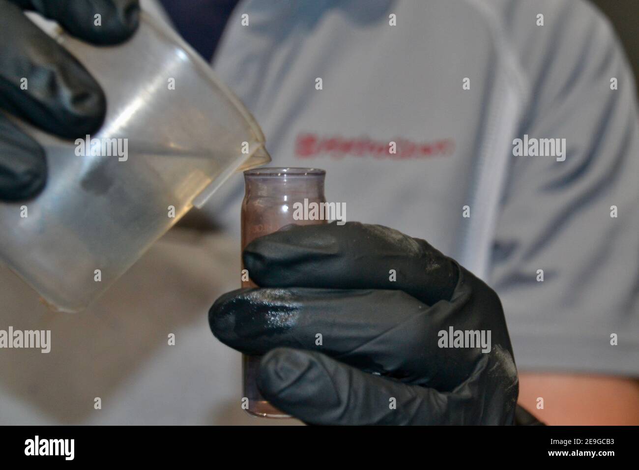 Chemiker mit Reagenzglas und Becher zur Prüfung der Wasserprobe Mit PSA-Gummihandschuhen in Nahaufnahme Stockfoto