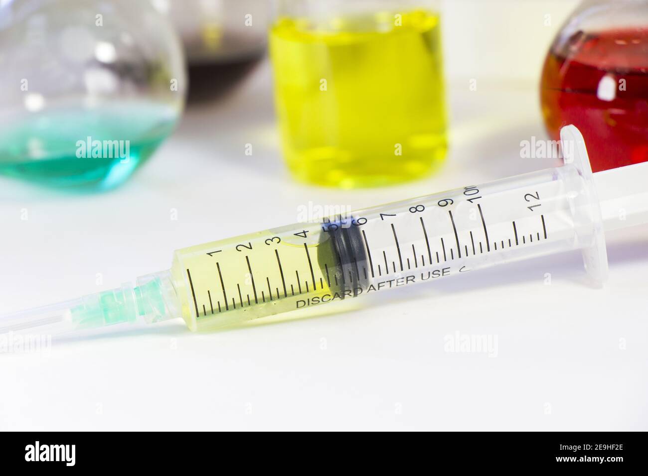 Nahaufnahme einer Spritzennadel mit dem Impfstoff auf dem Tabelle mit Chemikalien darauf Stockfoto