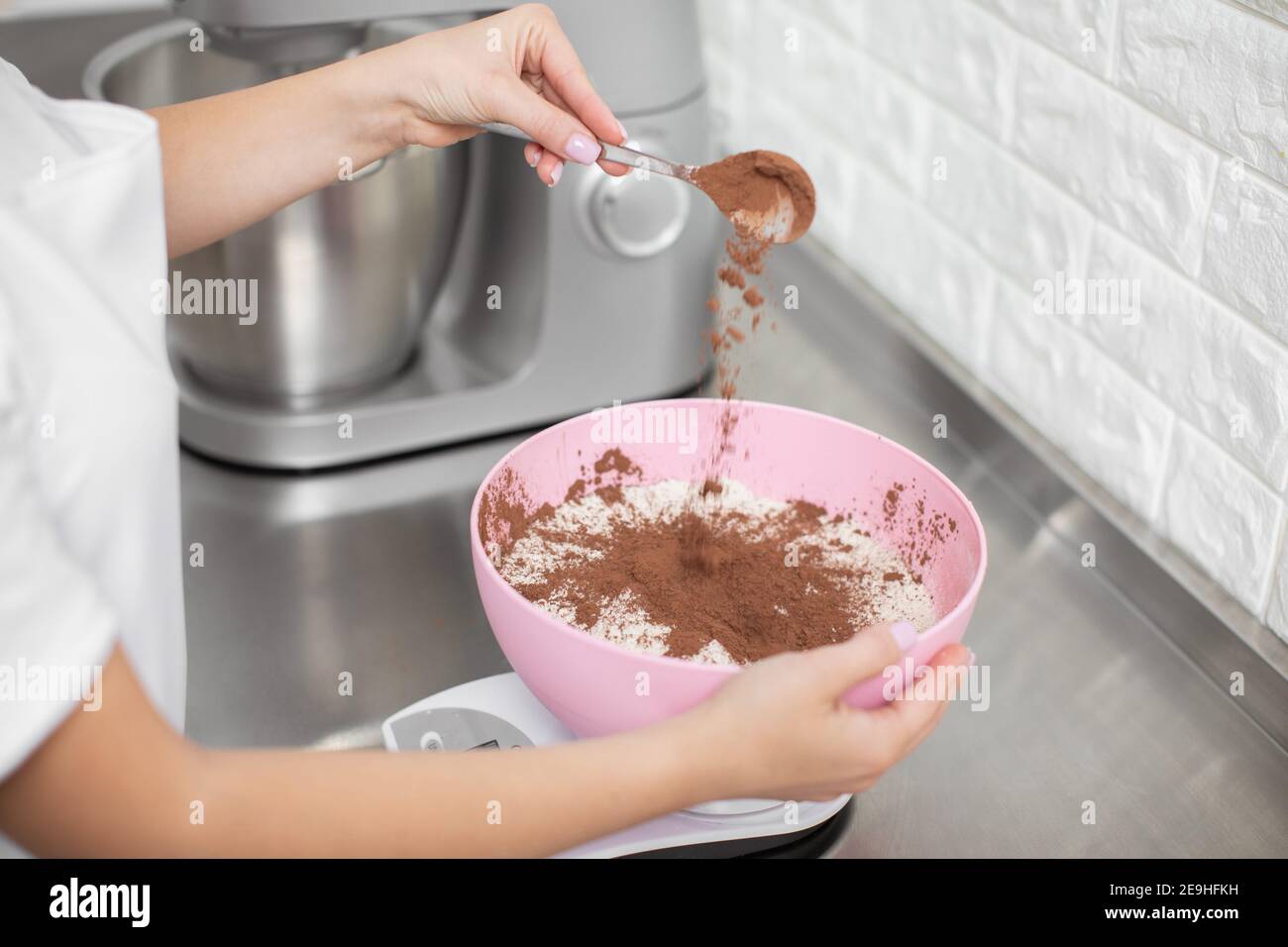 Nahaufnahme eines zugeschnittenen Schusses von Händen einer professionellen Küchenchefin, die Kakaopulver mit weißem Mehl in die Schüssel gießt. Makarons, Kuchen und Desserts Stockfoto