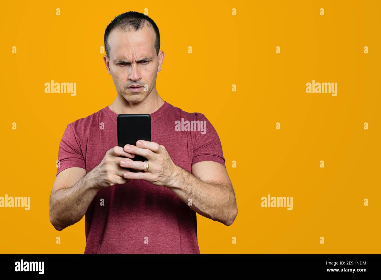 Reifer brasilianischer Mann, der sein Smartphone anschaut und ein missbilligendes Gesicht macht. Orangefarbener Hintergrund. Stockfoto